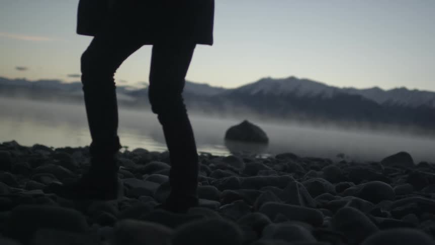 Person walking along a rocky shore next to a misty lake