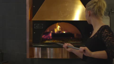 Woman cooks pizza in a large oven