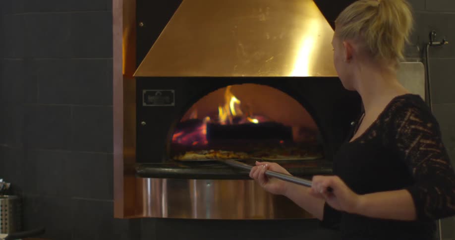 Woman cooks pizza in a large oven