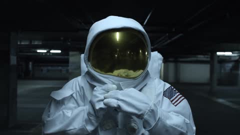 An astronaut pulling his visor down over his face and fastening the collar around his helmet