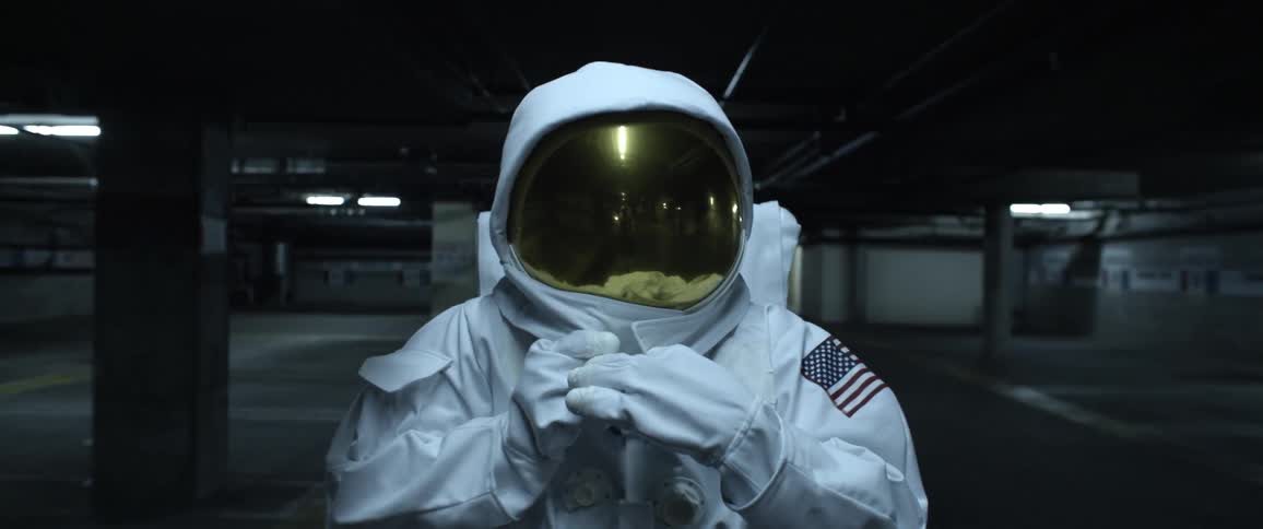 An astronaut pulling his visor down over his face and fastening the collar around his helmet