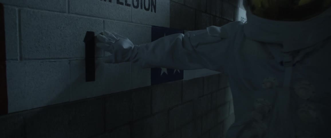A person wearing an astronaut costume touches a sign on the cinder block wall