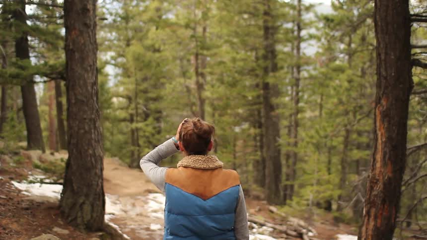 Woman looks around in forest during the day