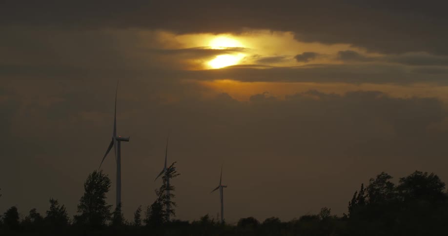 Three wind turbines spin slowly in the wind as the sun is obscured by clouds