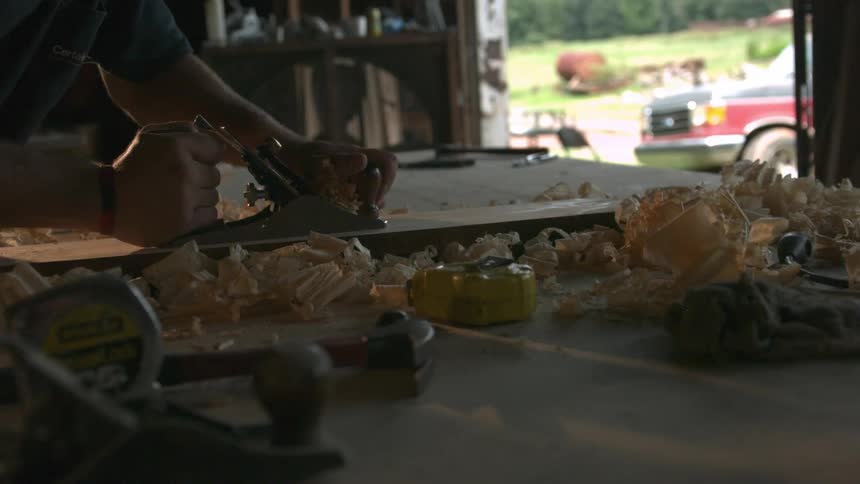 Man shaving bits of wood off a wooden board