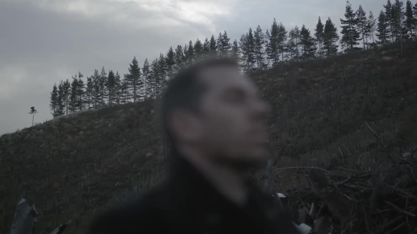 A man standing next to a steep hill looking upwards towards a sky filled with dark clouds