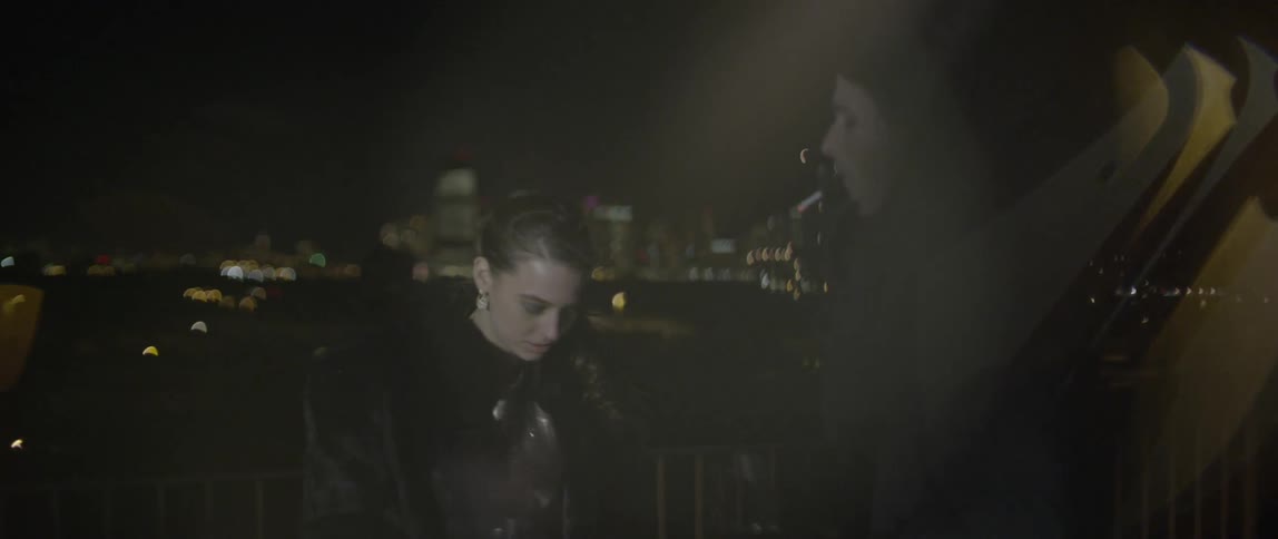 A young man and woman talking outside while the man smokes on a cold night in the city