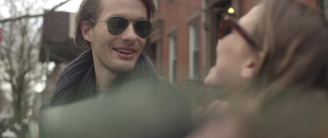 A young man and woman talking and laughing while she briefly rests her head on his chest as they stand on a city street