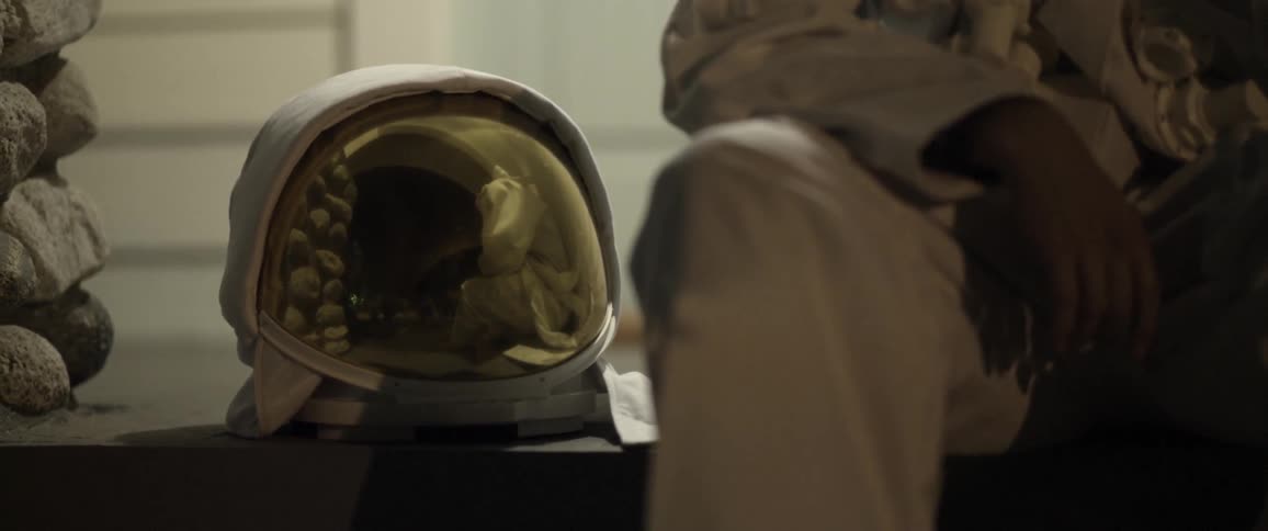 A man dressed as an astronaut sitting on a bench with his helmet next to him