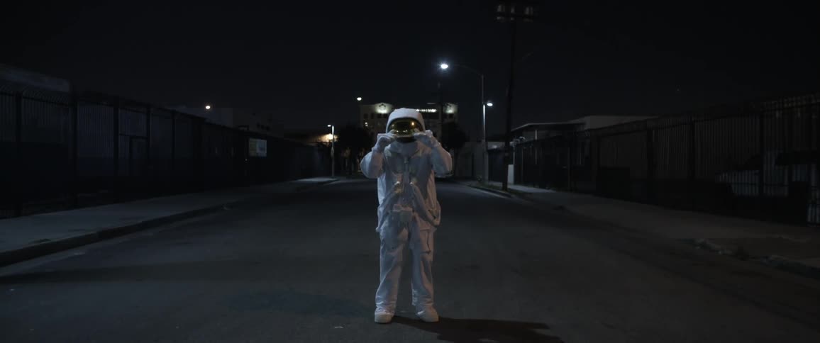 A person in an astronaut suit stands in the middle of an empty street at night