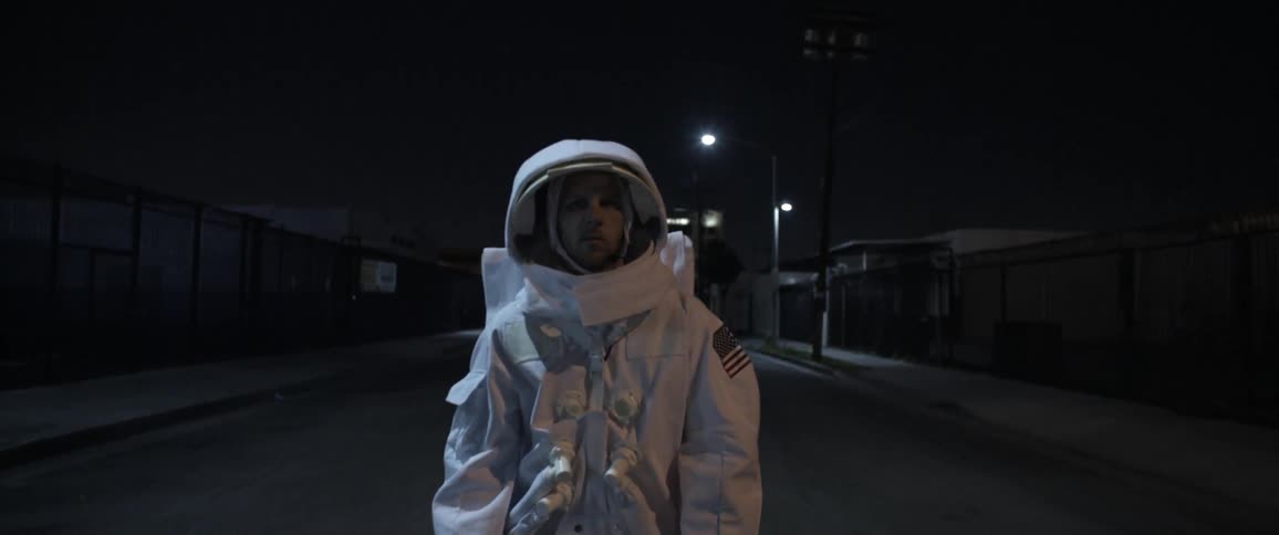 A man in an astronaut costume wanders down an empty urban street
