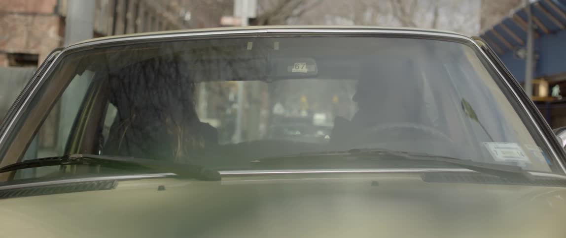 A man and a woman talking and laughing while sitting in a car that is parked on a city street