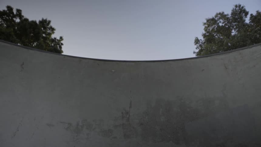 A young man rides a bicycle along the wall of a skate park