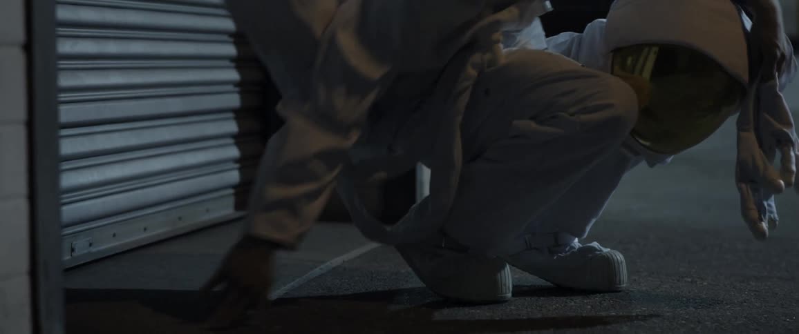A man dressed as an astronaut sitting on a sidewalk with his helmet on his knee before he stands up
