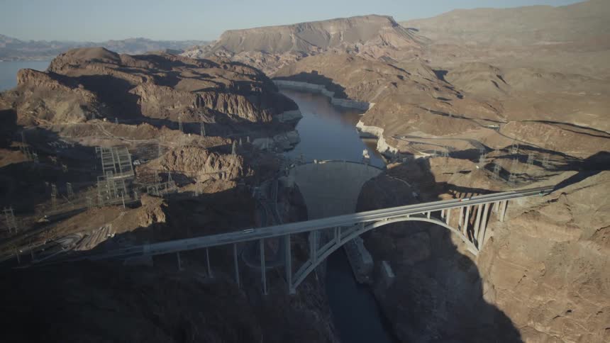 An aerial view of a bridge crossing a canyon river in a mountainous area