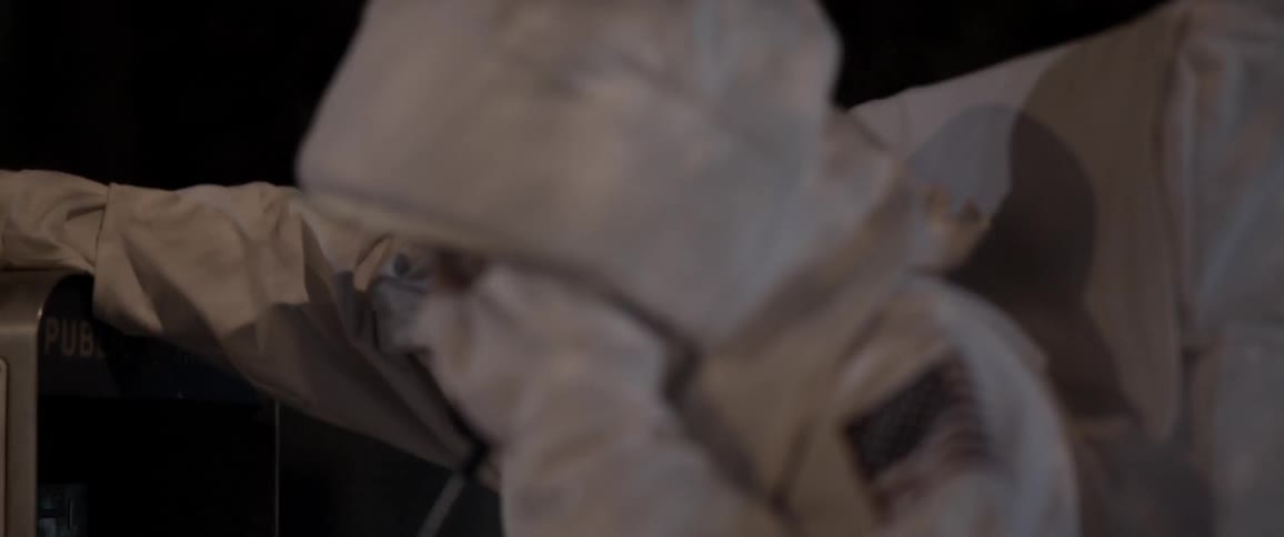 A man in an astronaut costume picks up the receiver at a phone booth and dials a number to make a call