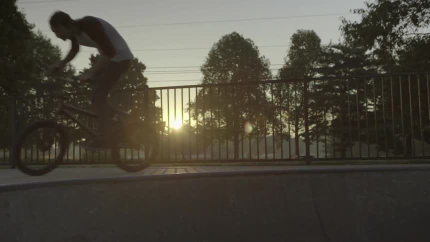 A boy riding a bicycle and doing a wheelie with a fence and trees in the background