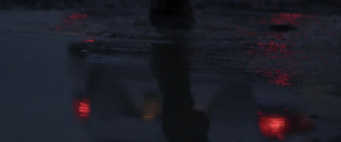 Person walks over a puddle of water away from a vehicle at night
