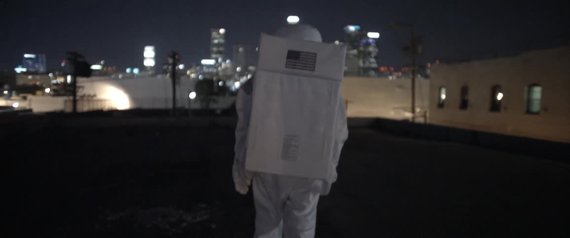 A man dressed as an astronaut walking on a rooftop in an urban area