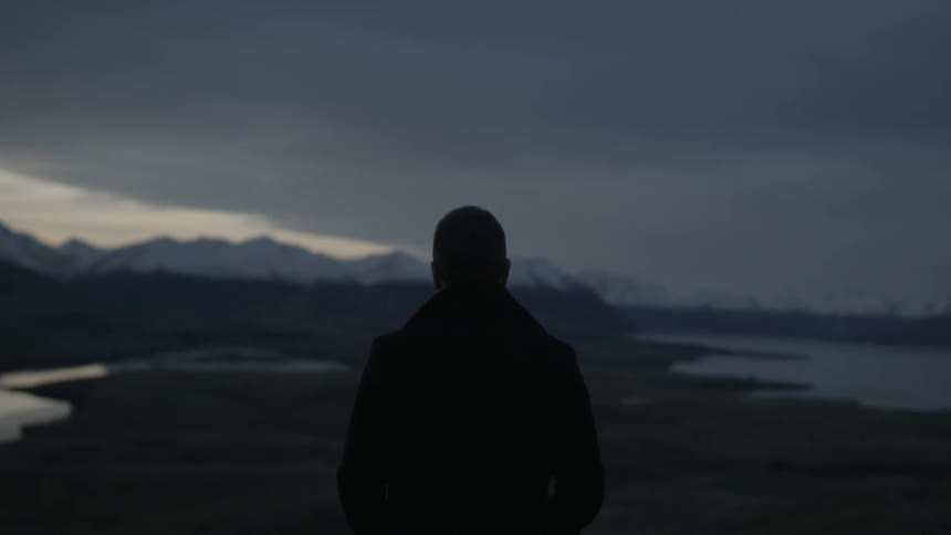 Man stands alone in a remote mountainous region at dusk
