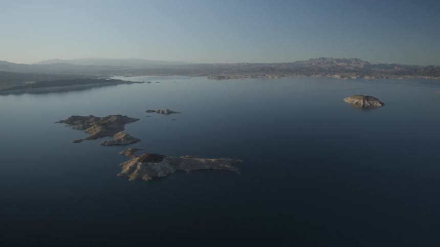 An aerial view of tiny island dotting a body of water with mountains in the background