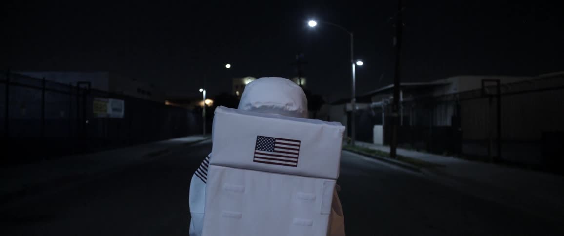 Person in a USA astronaut suit walks down a city street at night