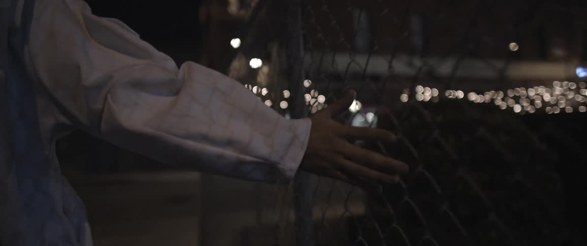 A person runs hand along a chain link fence in the city at night