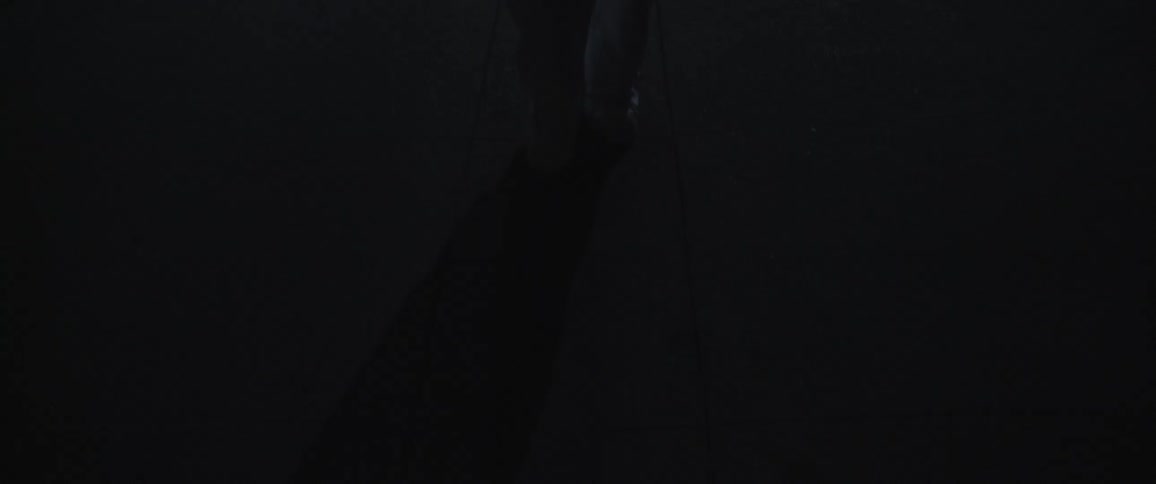 A man wearing white pants and shoes walks slowly at night
