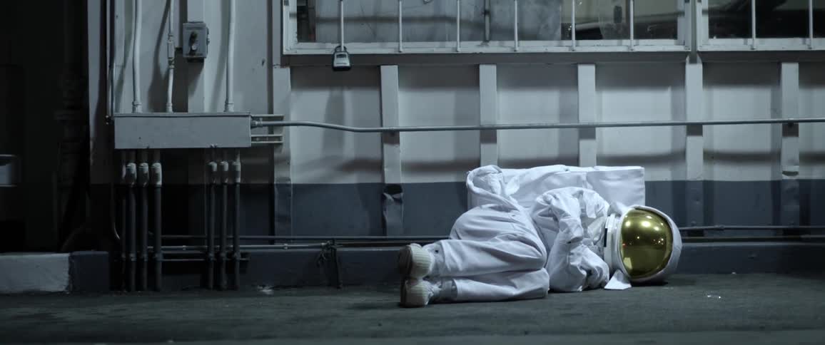 A person in an astronaut suit lying down on their side on the sidewalk