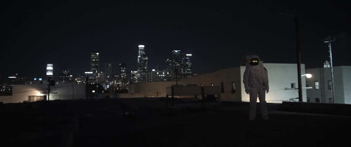 A man in an astronaut suit standing on a roof in the city at night