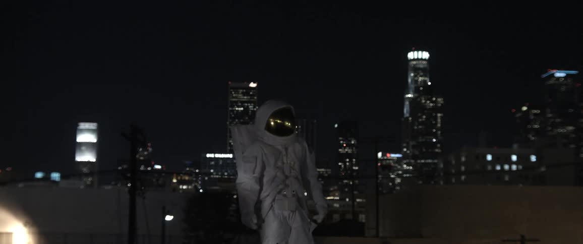 Man in spacesuit dancing at night outdoors in the city