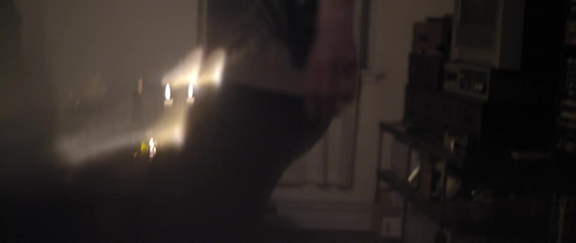 A man and woman dance at home while candles light up the background