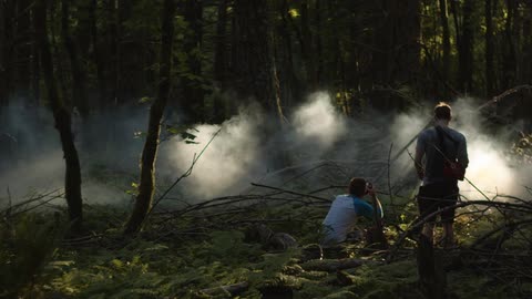 One man takes a picture of fog as another man stands by watching him