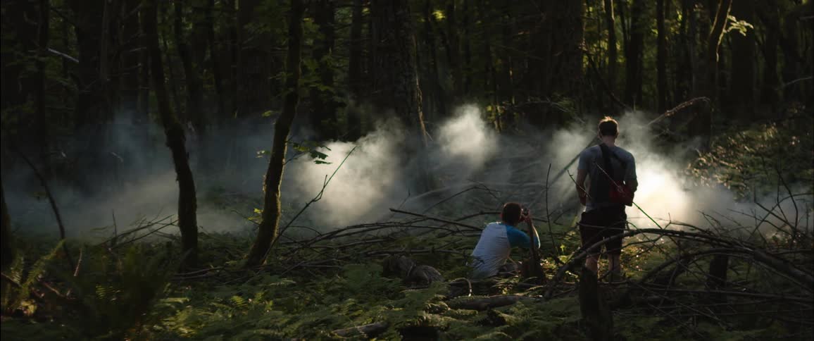 One man takes a picture of fog as another man stands by watching him