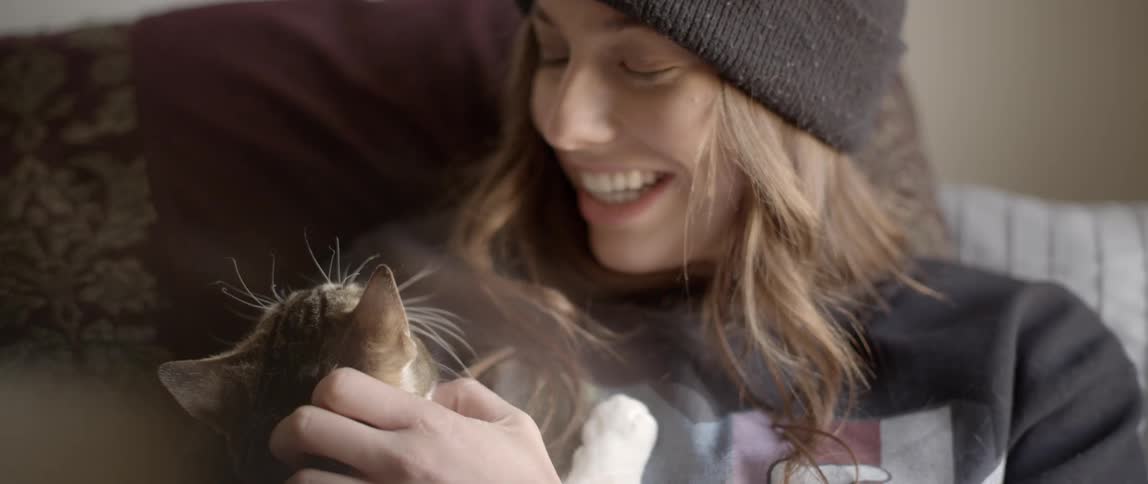 A blond woman in a knit cat cuddles and talks to a cat