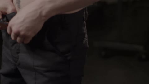 Shirtless man fastening up his pants indoors
