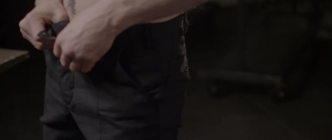 Shirtless man fastening up his pants indoors