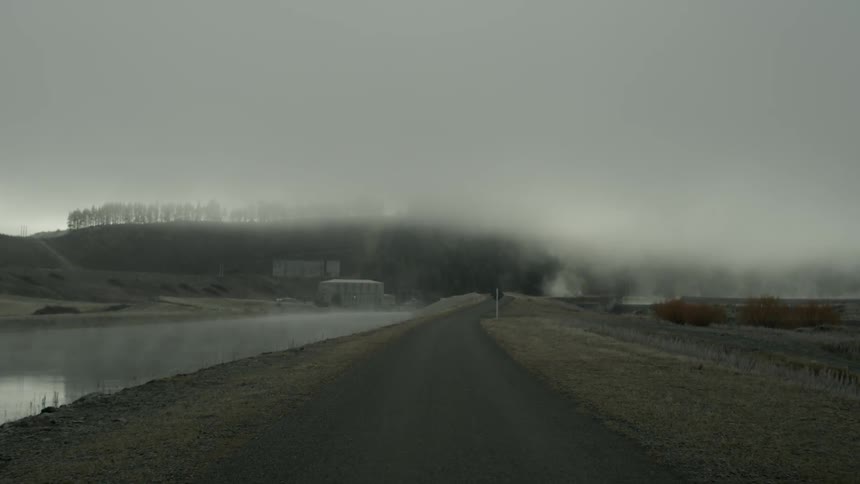 Long road near a stream with heavy fog in the distance