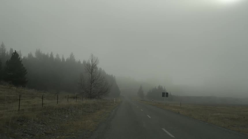 A vehicle drives down a foggy, rural road