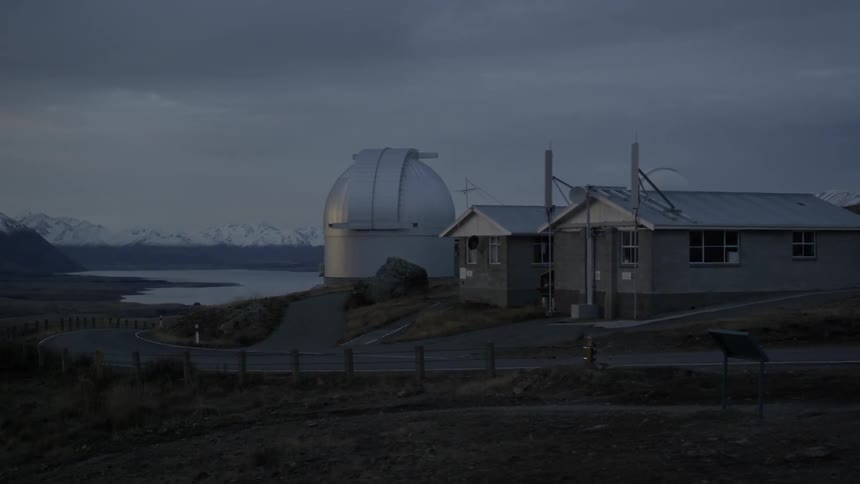 A large telescope sits near two buildings