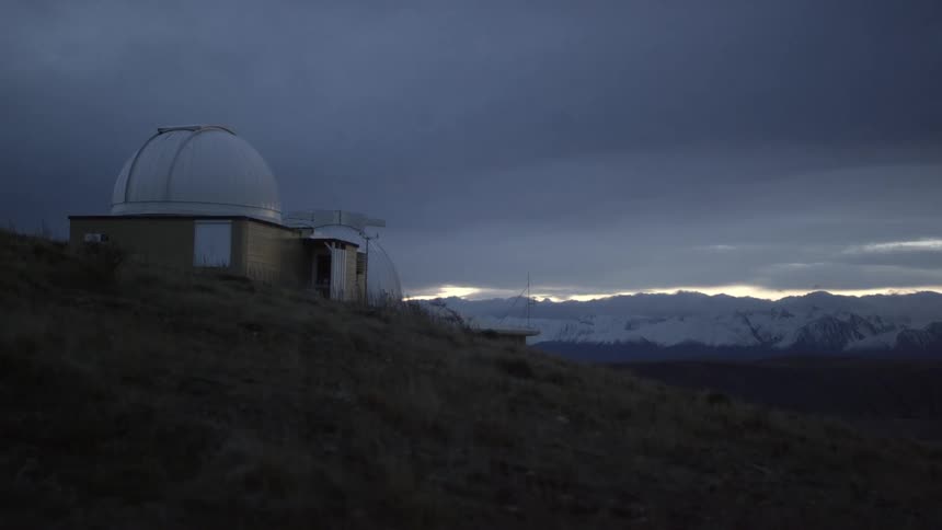 A domed building stands in front of snow-covered mountains