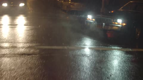 A car drives on city streets in the nighttime rain