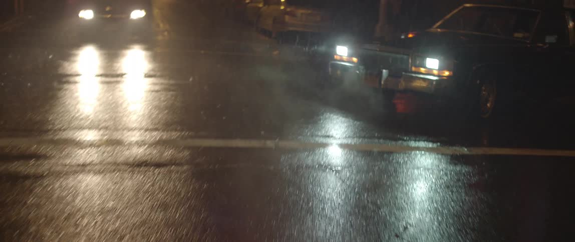 A car drives on city streets in the nighttime rain