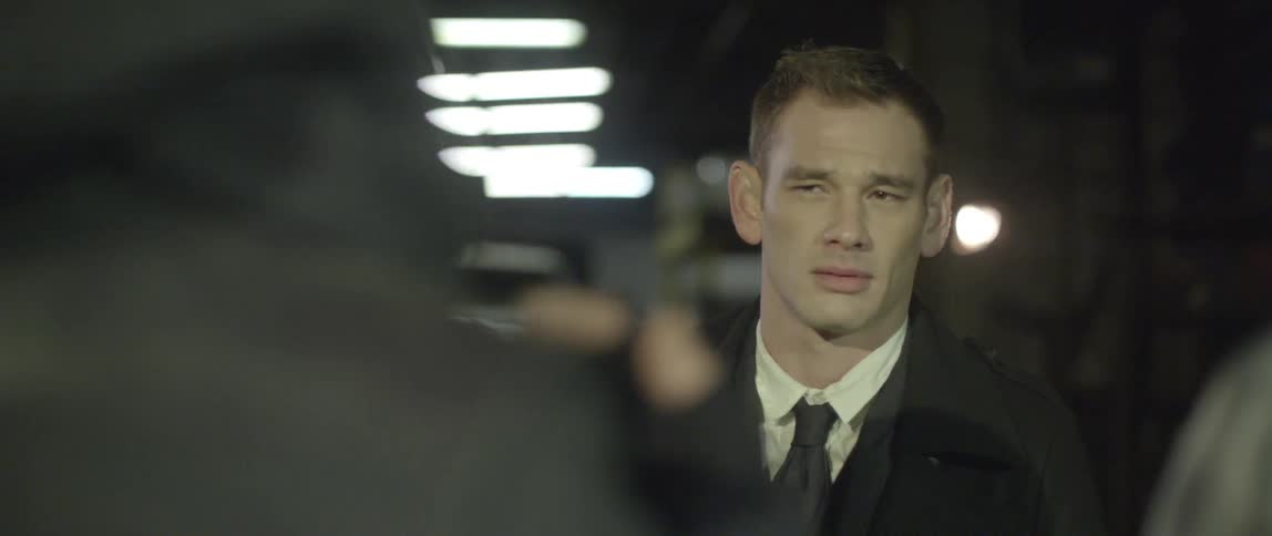 A man stares nervously at two people as one takes their hood off to reveal their face