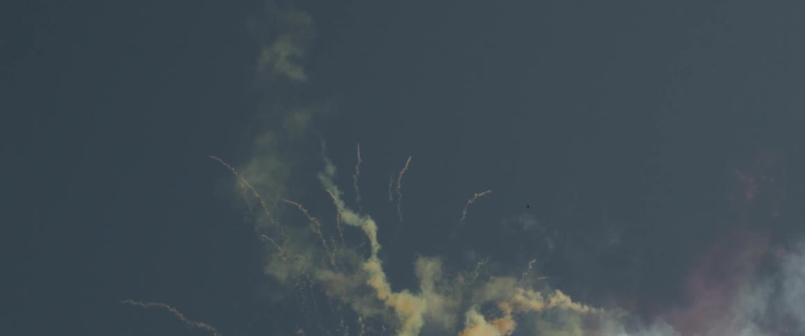 Colored smoke fills the blue sky