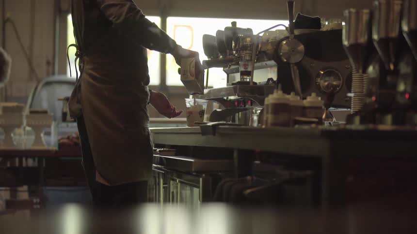 A man in a coffee shop wearing an apron and preparing a drink
