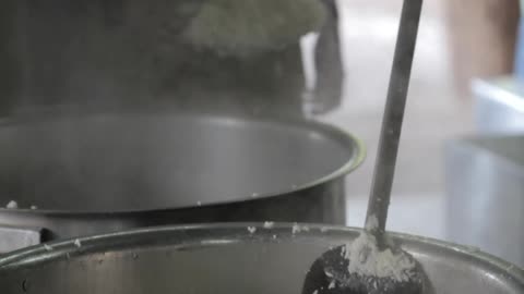 Workers prepare large vats of rice in a commercial kitchen