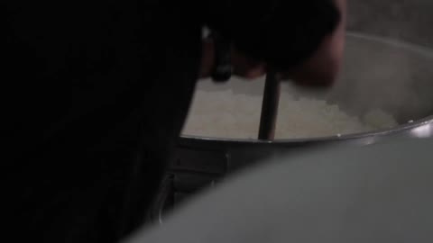 People mixing a large pot of rice
