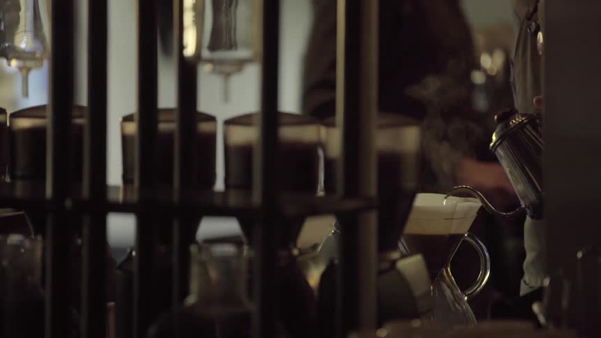 A man in a coffee shop pouring boiling water into a coffee filter