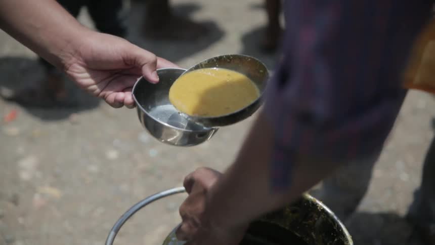 People being served soup into metal bowls from someone with a bucket